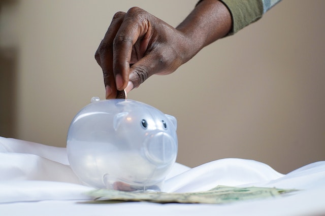 hand placing coins in a white piggy bank